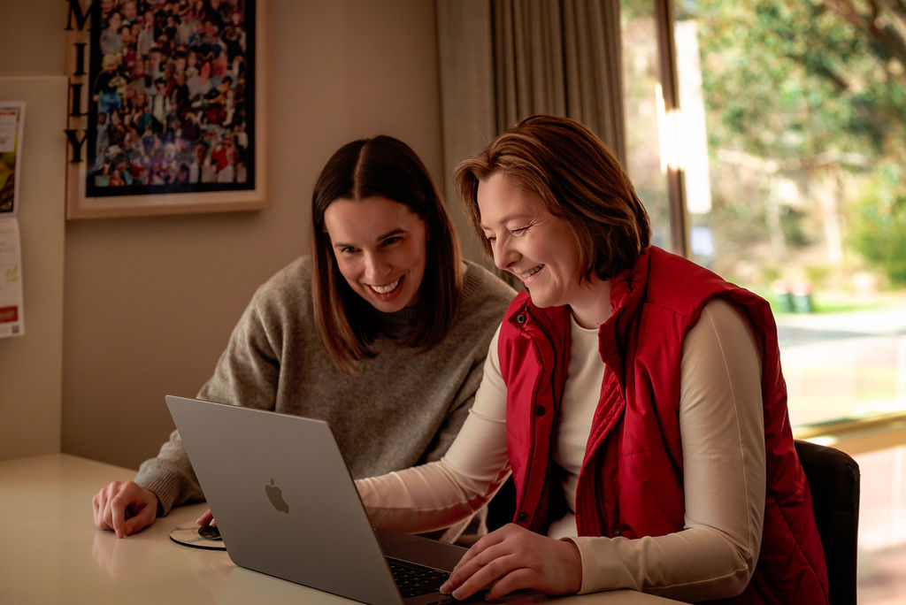 Support coordinator working with a person with disability, both smiling at a laptop